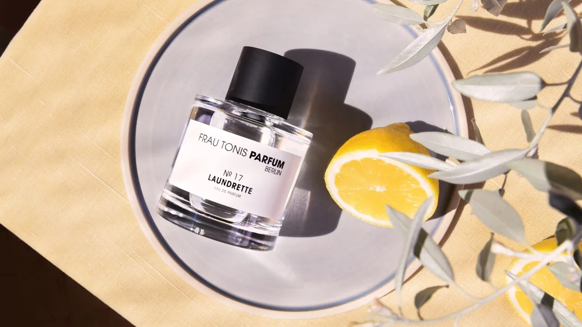 Flat lay of Frau Tonis perfume with citrus and olive branches, showcasing elegant Berlin-based fragrance.