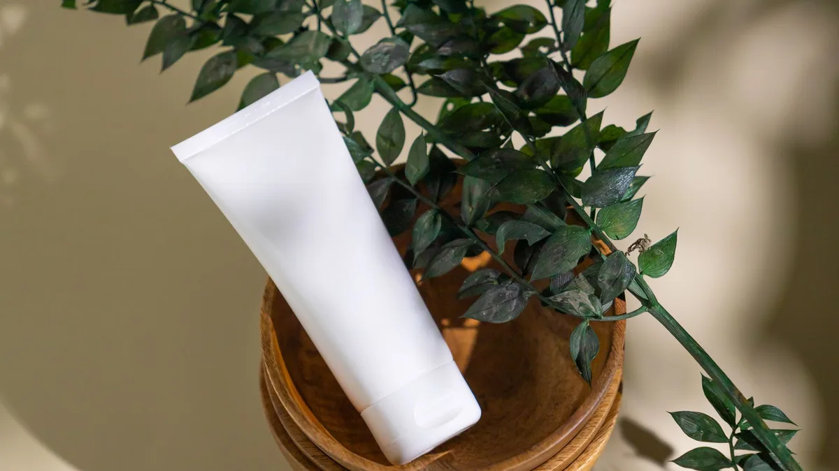 Minimalist skincare tube with green leaves in a wooden bowl, ideal for eco-friendly cosmetic themes.